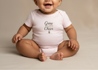 Baby wearing a white onesie with text, sitting on a beige background