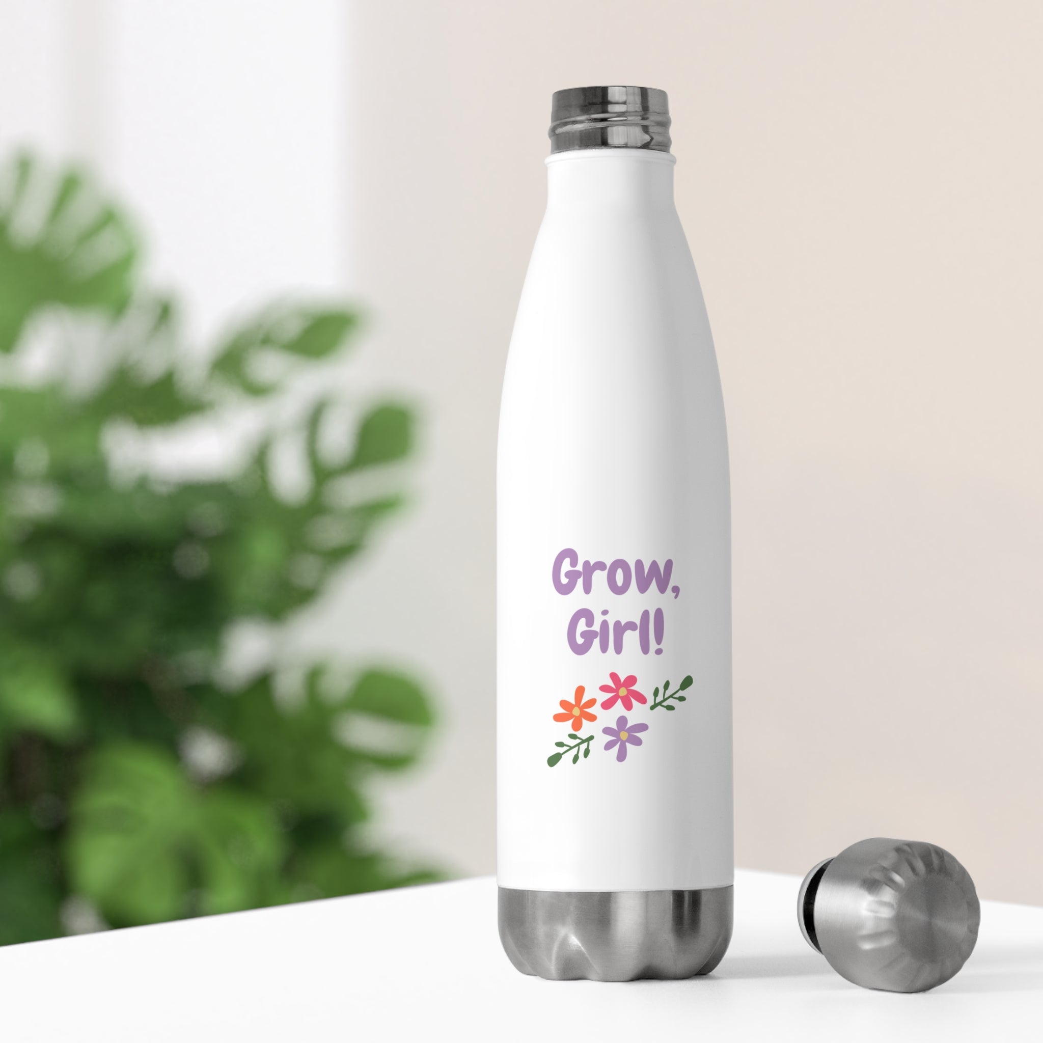 White insulated bottle with 'Grow, Girl!' text and floral designs on a blurred green plant background