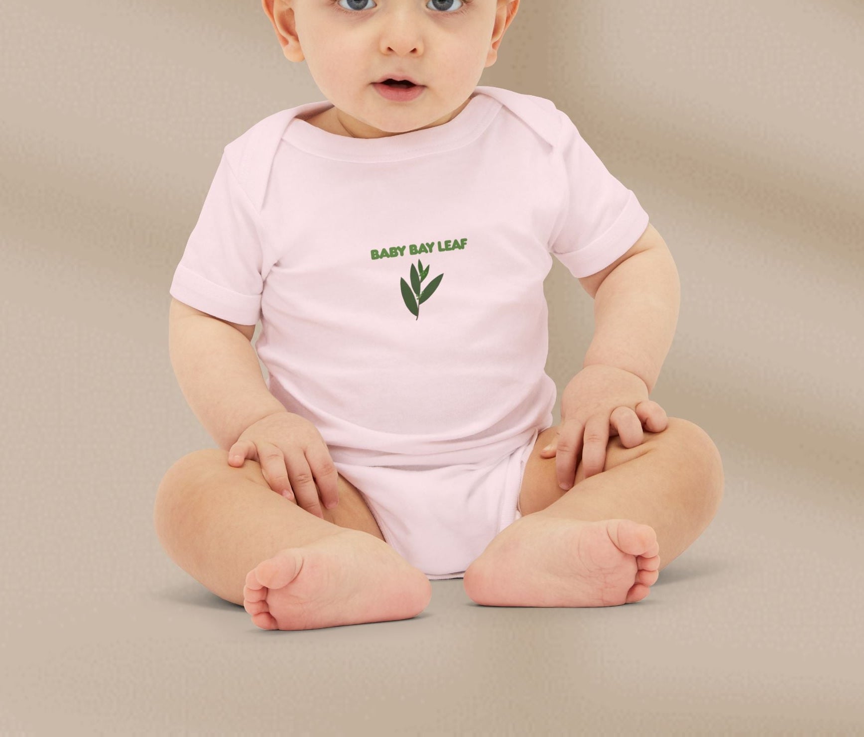 Baby wearing a pink onesie with 'Baby Bay Leaf' text and leaf design on a beige background