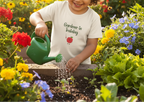 Child watering plants in a garden with a 'Gardener in Training' shirt.