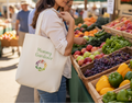 Woman shopping at an outdoor farmers market with a 'Mommy Gardener' tote bag.