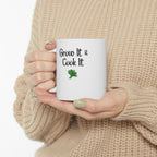 Person holding a white mug with 'Grow It & Cook It' text and a shamrock, wearing a beige sweater.