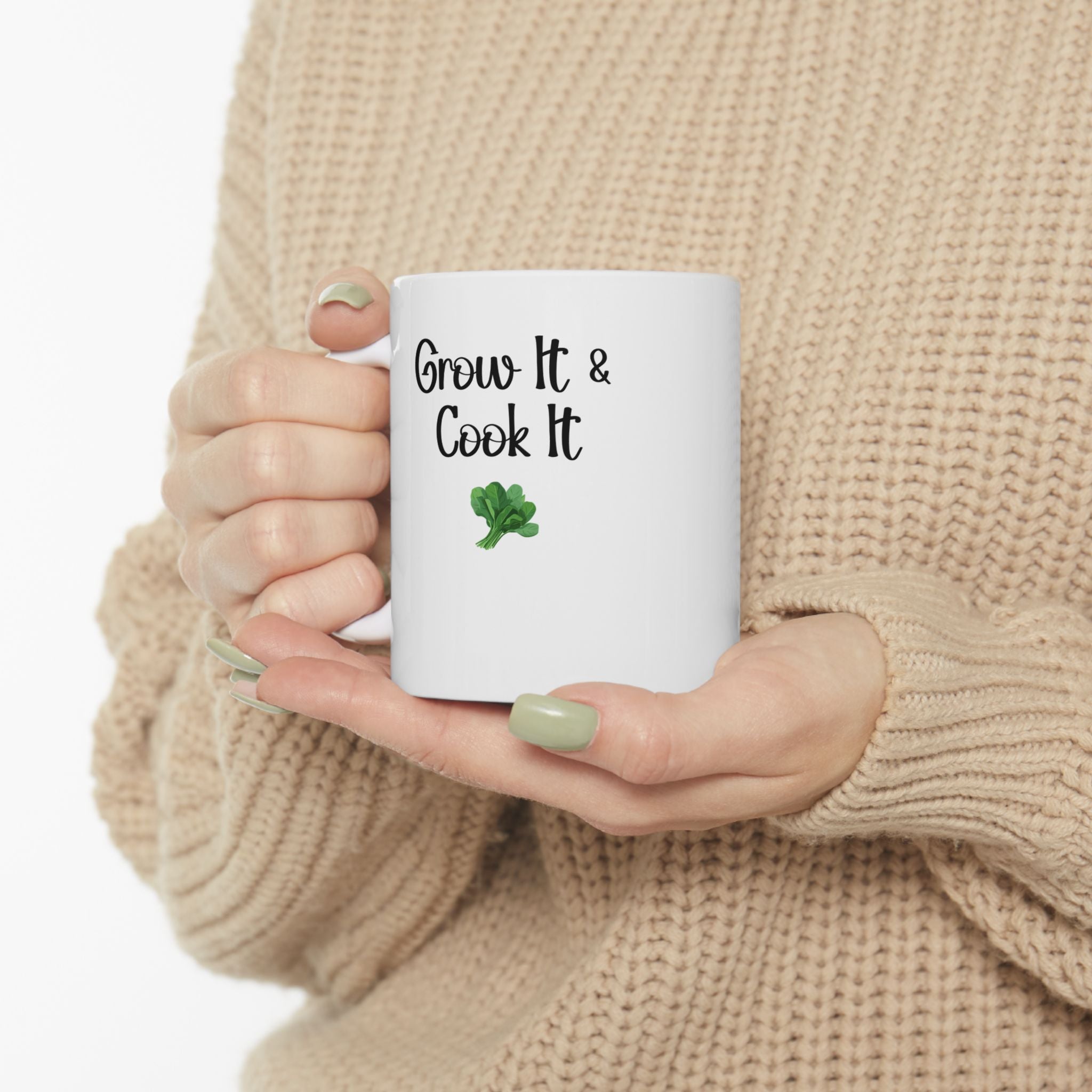 Person holding a white mug with 'Grow It & Cook It' text and a shamrock, wearing a beige sweater.