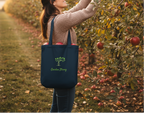Woman picking apples in an orchard with a tote bag labeled 'Garden Strong'.