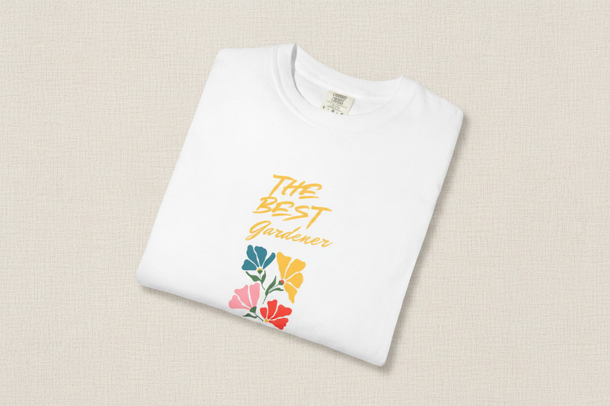White t-shirt with 'The Best Gardener' text and floral designs on a beige background