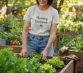 Woman in a garden wearing a 'Mommy Gardener' shirt, surrounded by plants and flowers.