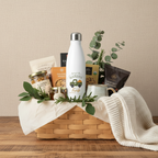 Gift basket with a water bottle, snacks, and a blanket on a wooden surface.