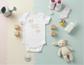 Baby clothing and items including a onesie, shoes, blocks, and a toy on a pastel background