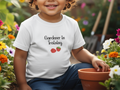 Child wearing a 'Gardener in Training' shirt in a garden setting