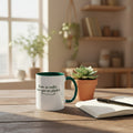White mug with green interior on a wooden table with a plant and notebook in a bright room.
