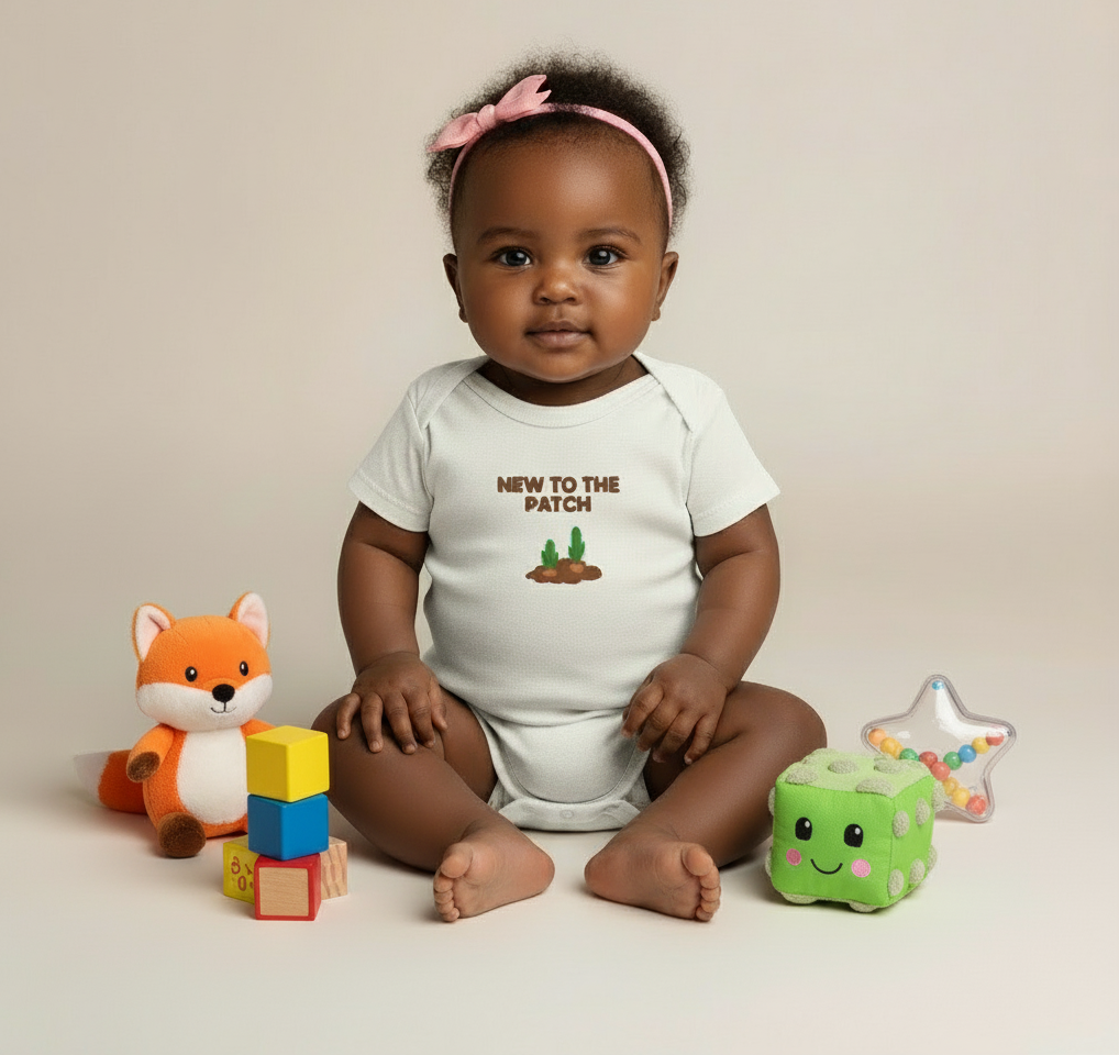 Baby wearing a onesie with text and graphics, surrounded by toys on a beige background