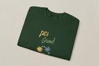 Folded green shirt with 'Let's Grow!' text and floral designs on a white background