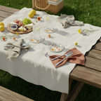 Outdoor picnic setup with a tablecloth, glasses, and food on a grassy background