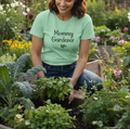 Woman in a garden wearing a 'Mommy Gardener' t-shirt, holding plants.