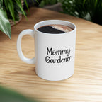 White mug with 'Mommy Gardener' text on a wooden table with coffee.