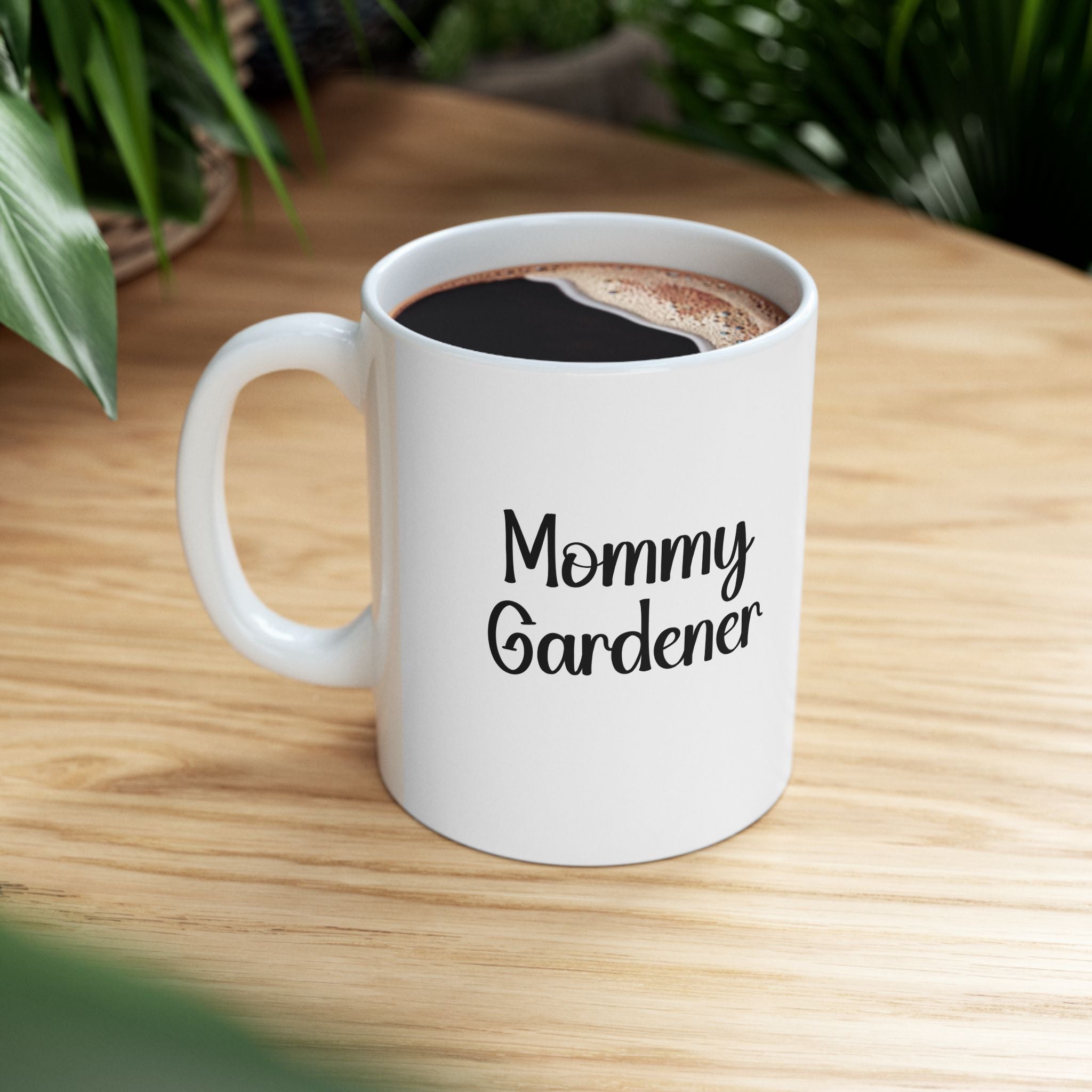 White mug with 'Mommy Gardener' text on a wooden table with coffee.