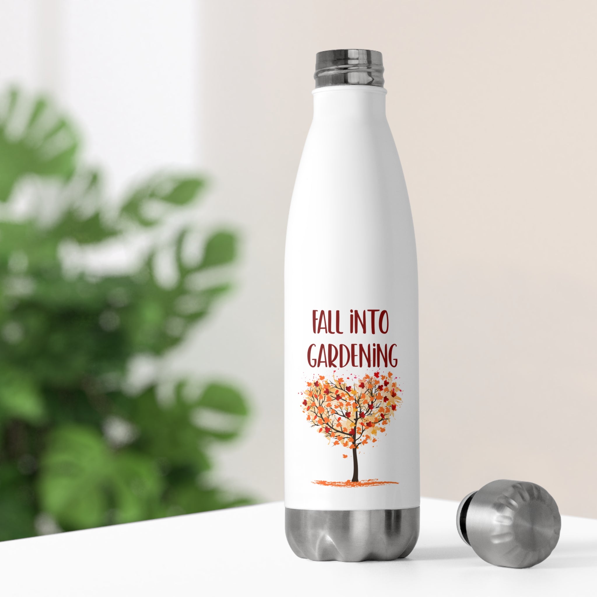 White water bottle with 'Fall into Gardening' design on a blurred green plant background
