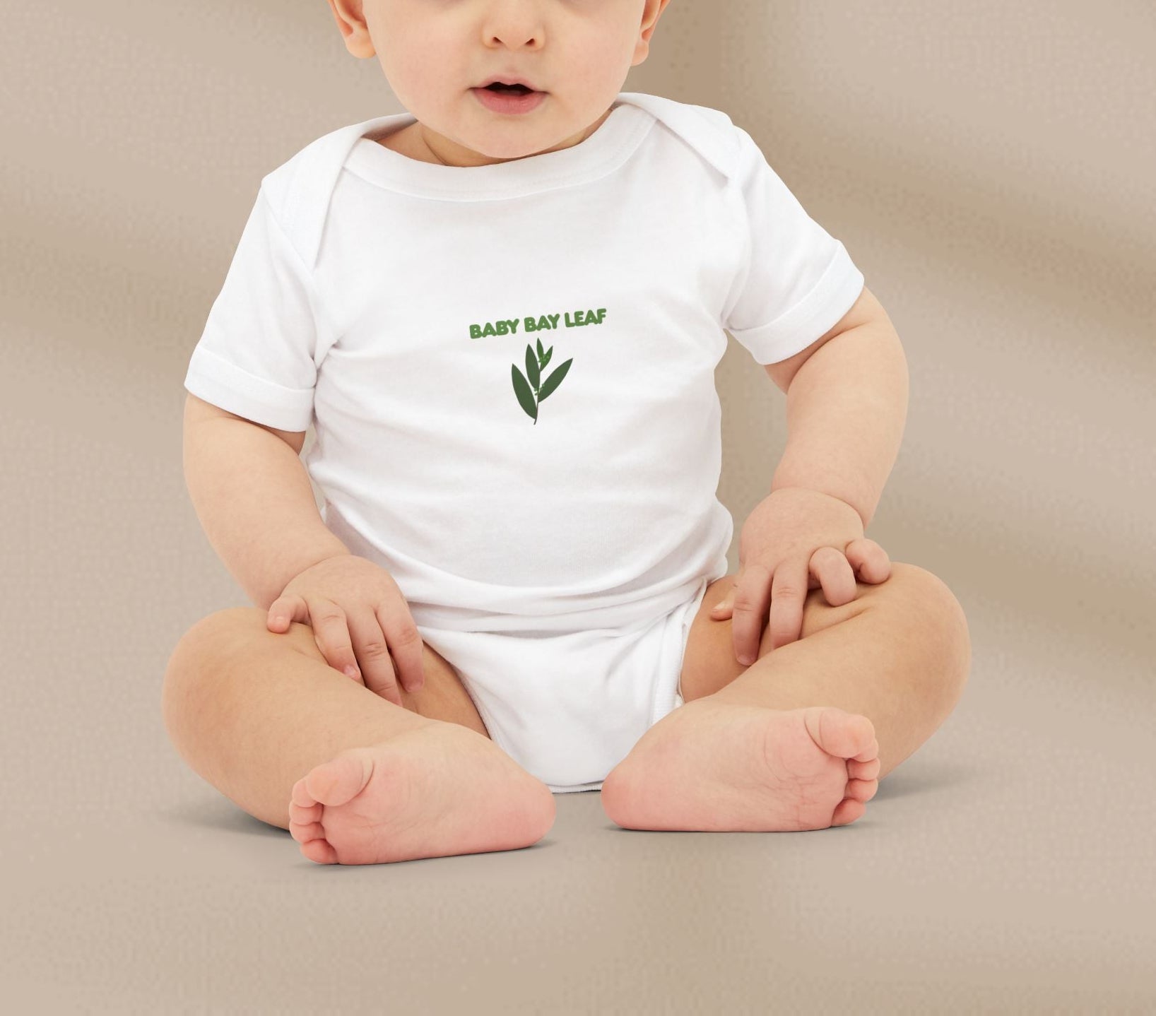 Baby wearing a white onesie with 'Baby Bay Leaf' text and leaf graphic on a beige background