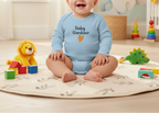 Baby wearing a blue 'Baby Gardener' onesie sitting on a rug with toys around.
