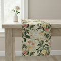 Floral table runner on a wooden table with a vase of flowers in the background.