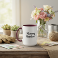 White mug with 'Mommy Gardener' text on a table with gardening accessories and flowers.