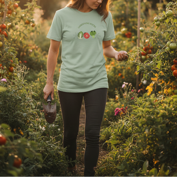 Person walking through a garden wearing a green t-shirt with a logo, holding a trowel.