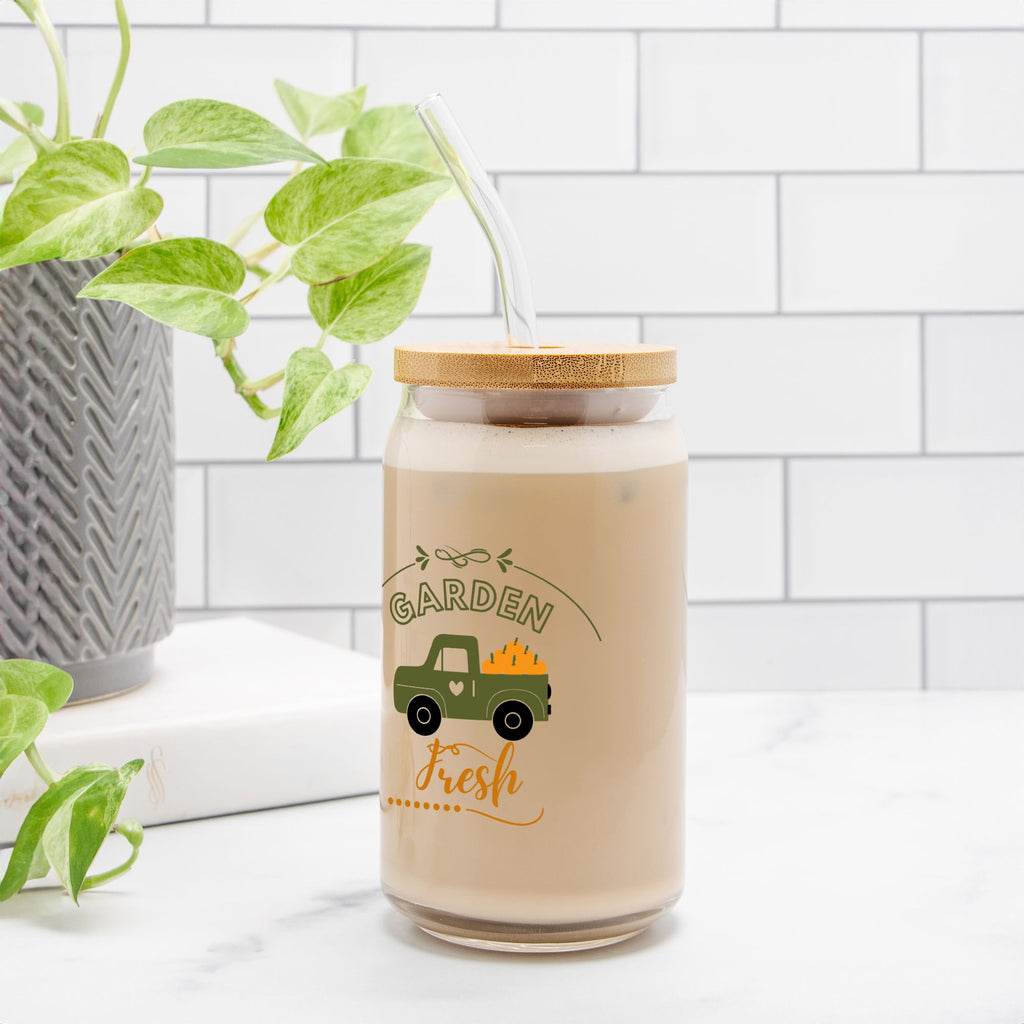 Glass jar with wooden lid labeled 'Garden Fresh' on a white surface with a plant in the background.