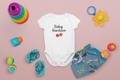 Baby onesie with 'Baby Gardener' text surrounded by colorful toys on a pink background