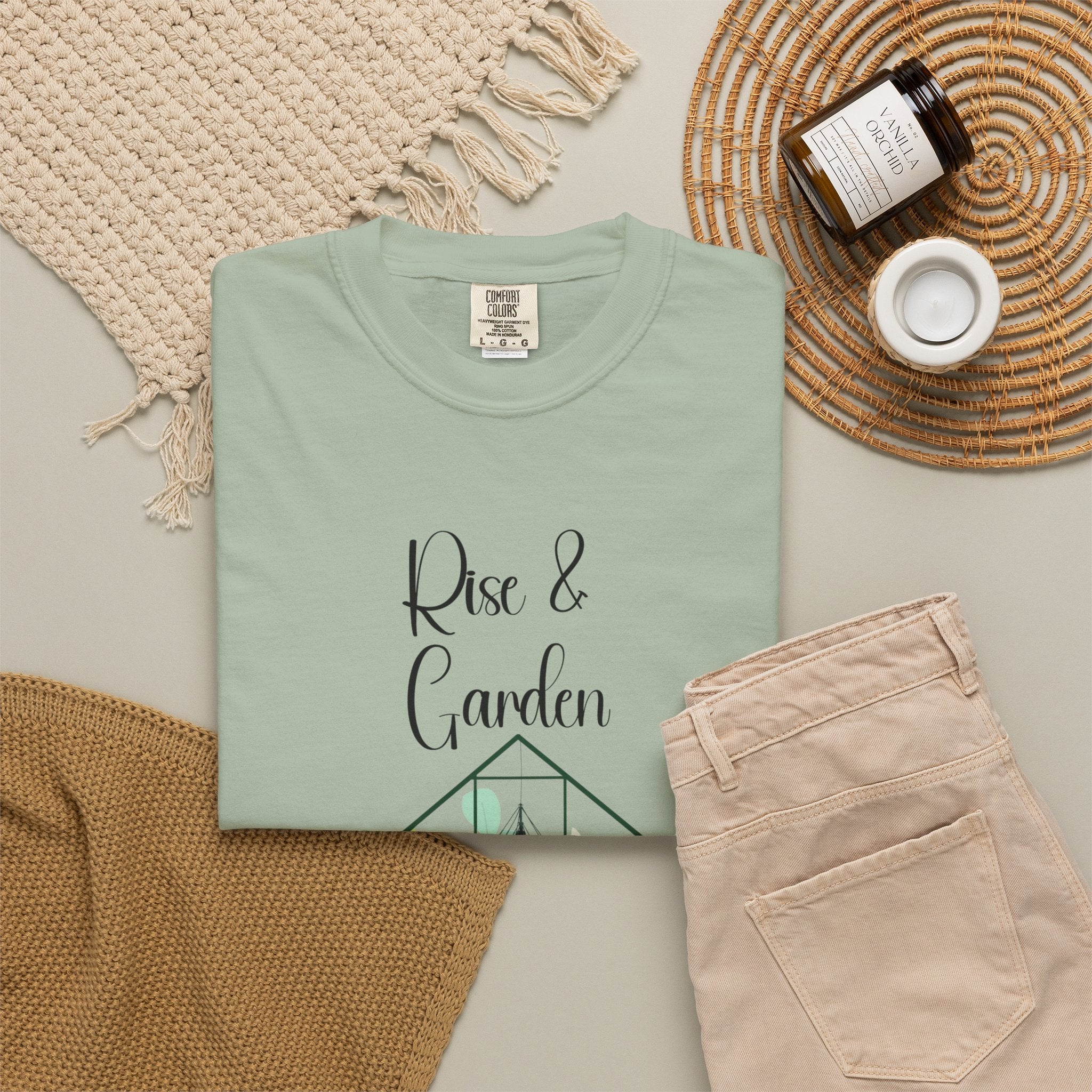 Folded mint green t-shirt with 'Rise & Garden' text on a neutral surface with accessories.