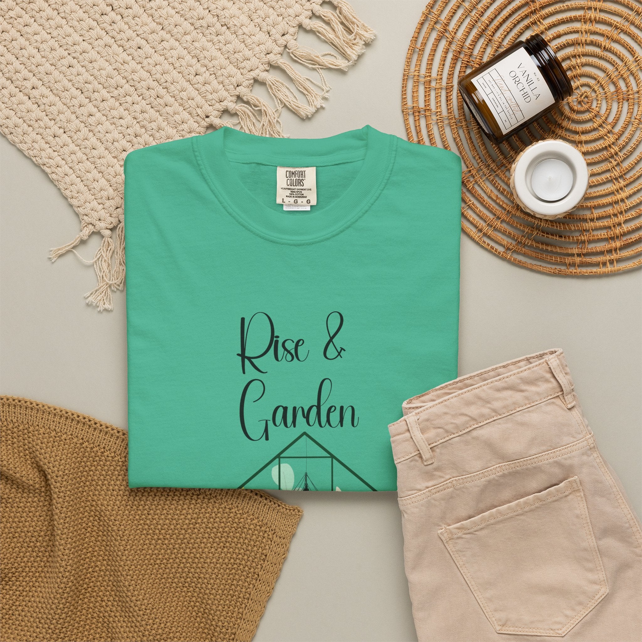 Green t-shirt with 'Rise & Garden' text on a neutral surface with accessories.
