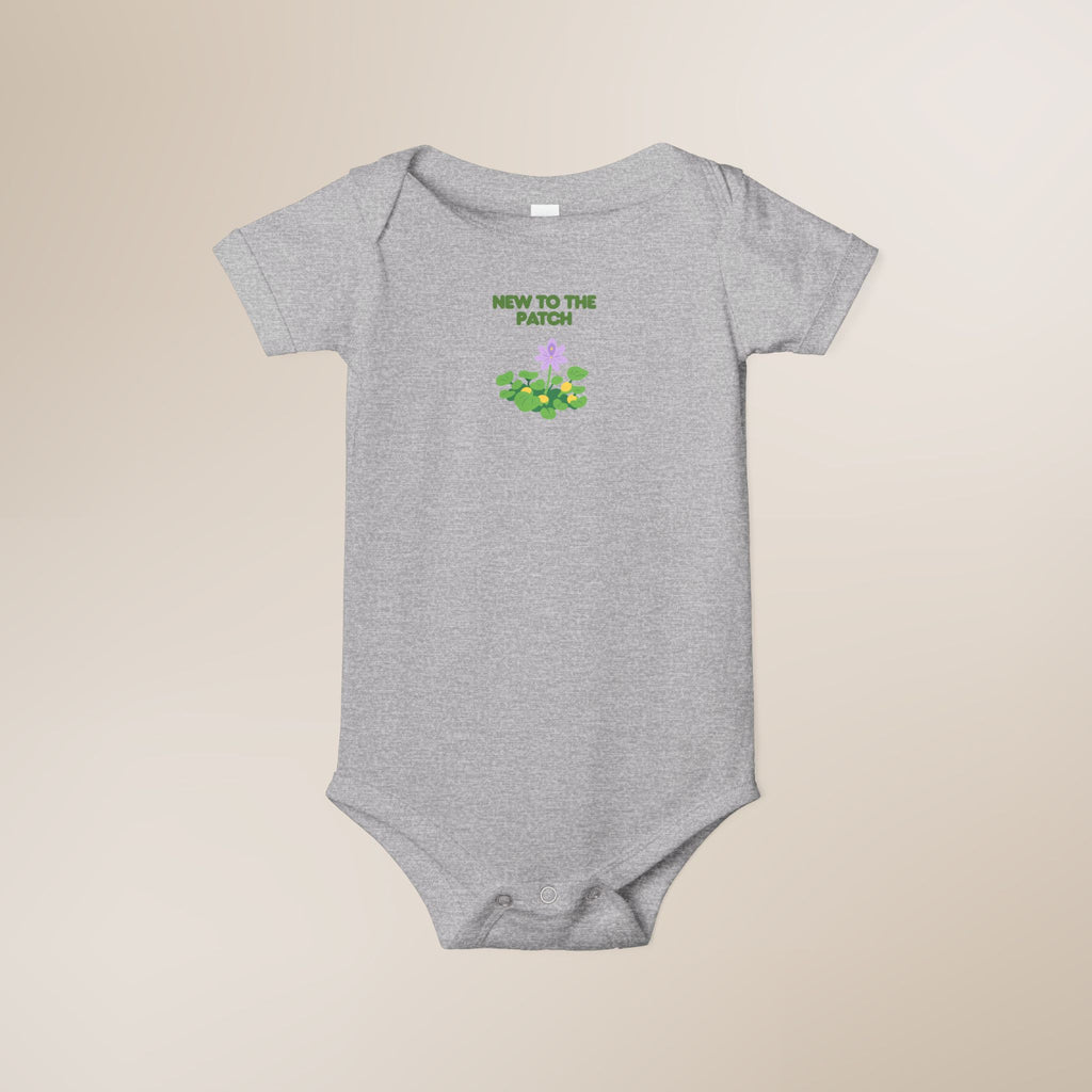 Gray baby onesie with 'New to the Patch' text and graphic on a beige background