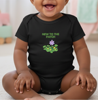 Baby wearing a black onesie with 'New to the Patch' text and flower graphic.