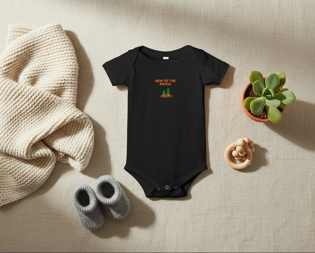 Black baby onesie with 'New to the Patch' text on a beige background