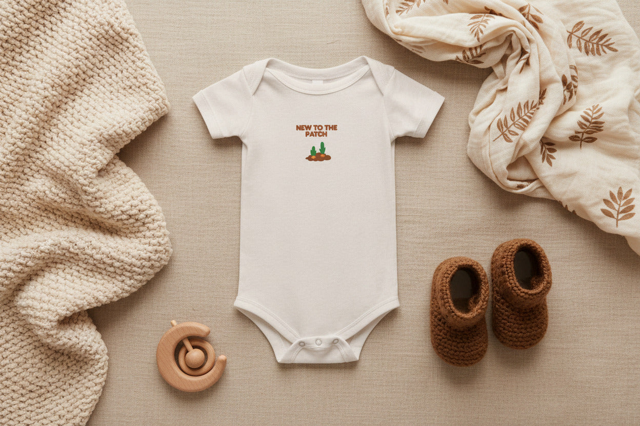 White baby onesie with 'New to the Patch' text and graphic on a beige background