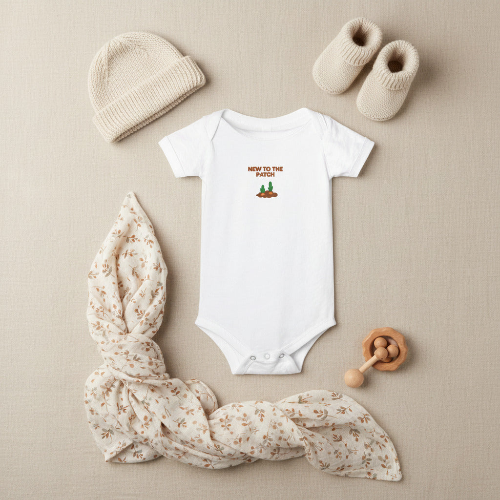 White baby onesie with 'New to the Patch' text and graphic on a beige background