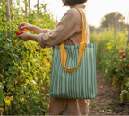 Person picking tomatoes in a garden with a green and yellow striped tote bag.