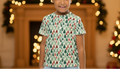 Child wearing a festive t-shirt with a Christmas tree pattern in a decorated room.