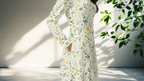 Person wearing a floral dress standing in a bright room with sunlight casting shadows.