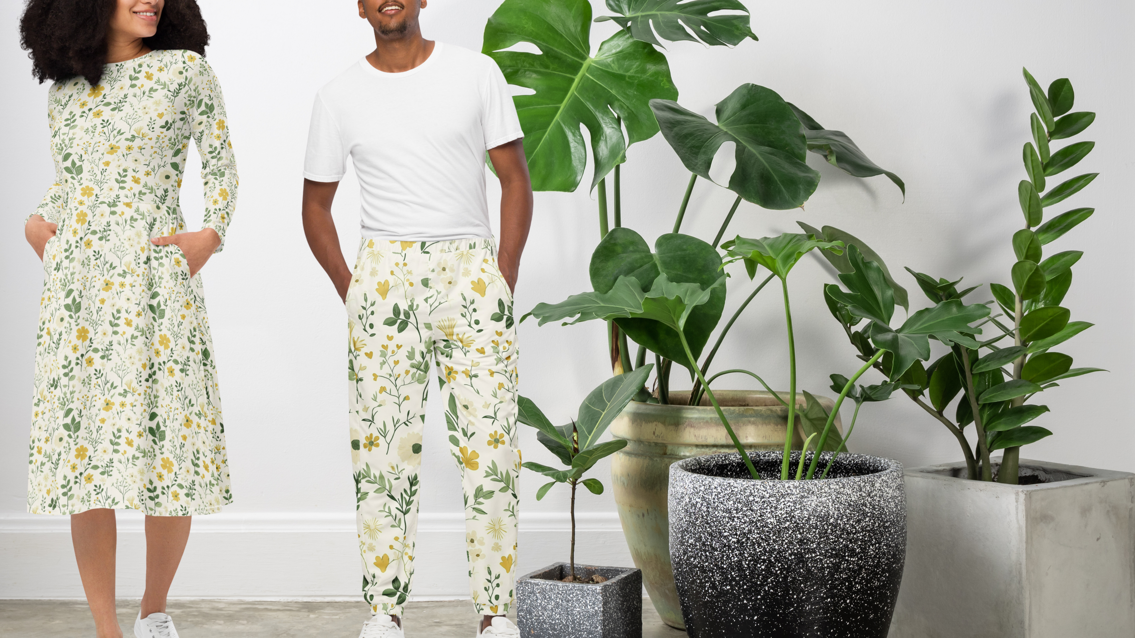 Two people wearing matching floral outfits standing in a room with potted plants.