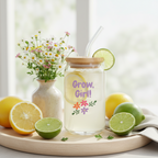 Glass jar with a straw, lemon slices, and lime on a wooden tray with flowers in the background.