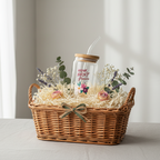 Gift basket with a glass tumbler and flowers on a light surface.