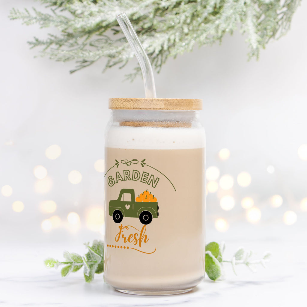 Jar with lid and straw, featuring a truck and 'Garden Fresh' text, on a white background with blurred lights and greenery.
