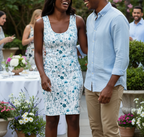 Woman in a floral dress standing next to a man in a light blue shirt at an outdoor event with flowers and people in the background.