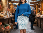 Woman in a blue sweater and floral skirt standing in a snowy outdoor market.