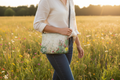 Person holding a floral-patterned handbag in a field of wildflowers