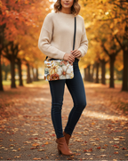 Woman in beige sweater and dark jeans holding a floral clutch in an autumn park.