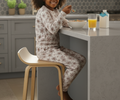 Child in pajamas sitting on a stool at a kitchen counter eating cereal with a glass of orange juice.
