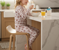Child sitting on a stool at a kitchen counter eating cereal with a glass of orange juice and a carton of milk.