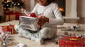 Child opening a gift in a festive setting with Christmas decorations.