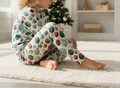 Child wearing polka dot pajamas sitting on a carpeted floor with a Christmas tree in the background.